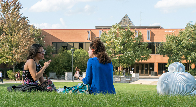Two female students sitting on the campus lawn
